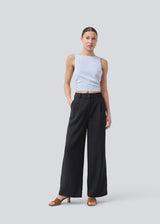 The sleeveless top is satin and light gray'ish blue. TailorMD top has an open back with a tieband. The model is 177 cm and wears a size S/36.