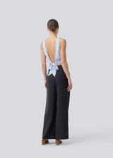 The sleeveless top is satin and light gray'ish blue. TailorMD top has an open back with a tieband. The model is 177 cm and wears a size S/36.