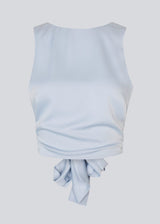 The sleeveless top is satin and light gray'ish blue. TailorMD top has an open back with a tieband. The model is 177 cm and wears a size S/36.