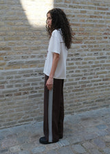 Loose brown trousers with wide legs and a relaxed fit. Featuring an elastic waistband with drawstring for a comfortable, adjustable waist. White side stripes add a sporty and modern touch to the otherwise classic design. Perfect for casual everyday wear or more elevated styling – easy to pair with everything from t-shirts to dressy tops.