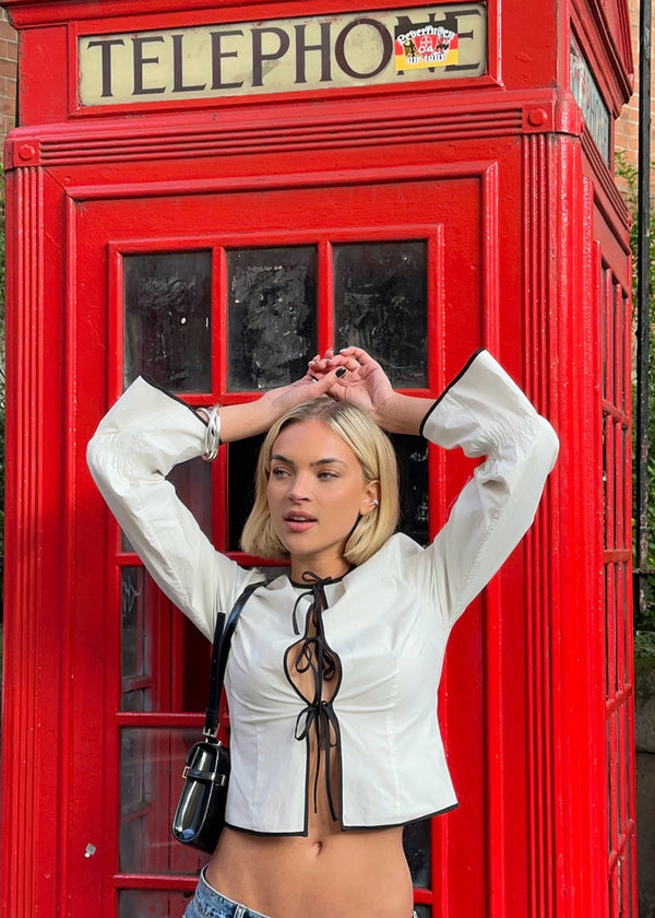 Fitted top in white with long loose sleeves. EmiliaMD shirt is closed with three black tie bands in front and has a ruffle detail at the sleeve. The model is 175 cm and wears a size S/36.