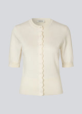 Feminine short-sleeved cardigan in lightweight knit. The Bennamd SS Cardigan features classic details such as ribbed trims, a button closure, and a round neckline, with a delicate wavy edge along the button placket for an elegant touch.