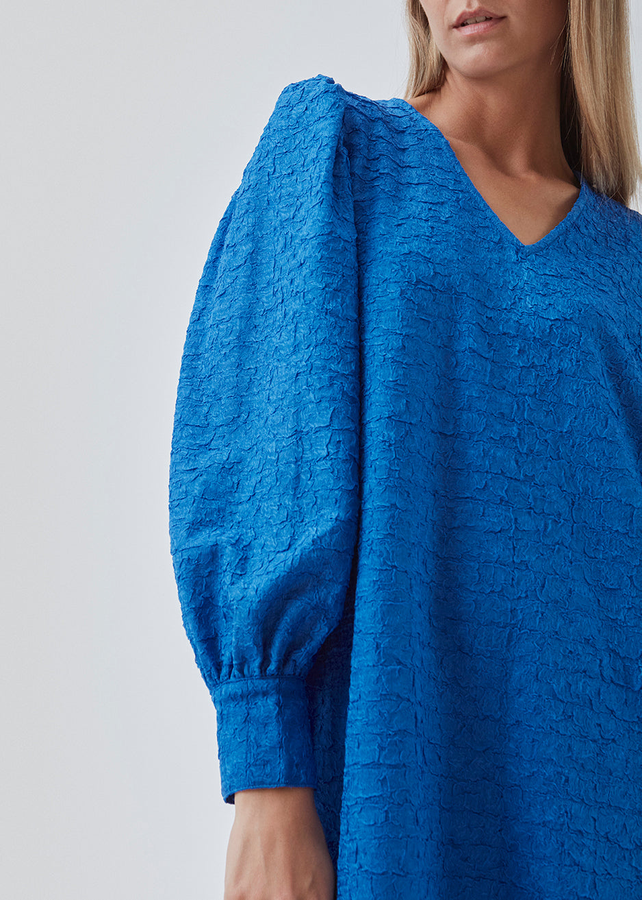 Minidress in blue with long volume sleeves a cuff. BisouMD dress has a v-neckline and an a-shaped silhouette in the body. The model is 176 cm and wears a size S/36