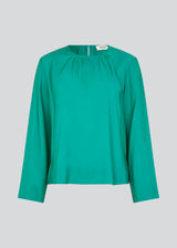 ChristopherMD top in green has a regular body with a round neck with gatherings, and small opening with button closure in the back. Long, wide sleeves. The model is 175 cm and wears a size S/36.