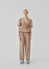 Beige top made from a cotton mix with short, slightly puffed, sleeves, and a deep v-neckline. DeenMD top has a flattering ruched detail below the chest and at the waist. The model is 177 cm and wears a size S/36.