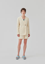 DimeMD blazer is designed in a textured cotton blend with lining. The blazer is collarless but has an asymmetrical wrap detail with a single visible button. The model is 177 cm and wears a size S/36. Style the blazer with matching shorts: DimeMD shorts.