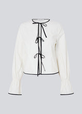 Fitted top in white with long loose sleeves. EmiliaMD shirt is closed with tree black tie bands in front and has a ruffle detail at the sleeve.