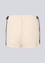 Cute shorts in a soft lace material in light beige/white. EmiliaMD lace shorts have lining and elastic at the waist. The shorts have two black bows on hips as a cool contrast to the light beige.