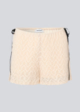 Cute shorts in a soft lace material in light beige/white. EmiliaMD lace shorts have lining and elastic at the waist. The shorts have two black bows on hips as a cool contrast to the light beige.