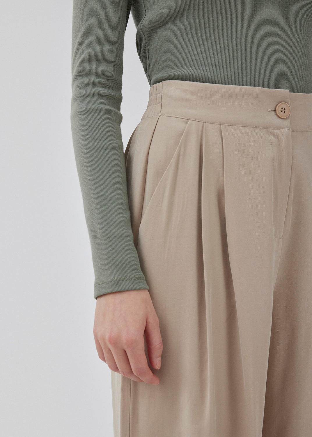 FanyaMD pants in bright beige have a menswear-inspired look with straight, wide legs, a high waist with zip fly and button and elastication in back. Doubble pleat in front and side pockets. The model is 175 cm and wears a size S/36.