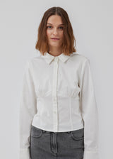 Form-fitting shirt in white in a woven cotton blend with collar, buttons in front, and long sleeves with cuff. HarrisonMD shirt has darts and a cutline below the chest for a corset-inspired look. The model is 175 cm and wears a size S/36.