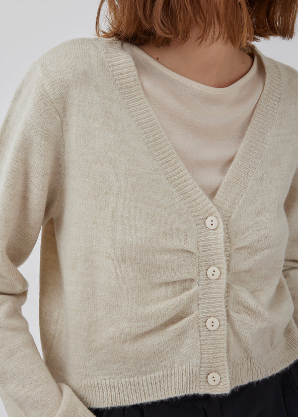 Cropped cardigan in beige in a soft material. HeatMD cardigan has a v-neckline and button closure in front with ruching. The sleeves are long. The model is 175 cm and wears a size S/36.