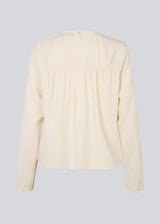 HiltonMD top in beige is designed with a relaxed fit, long sleeves and a round neckline with a hidden zipper at the back. The top is detailed with a ruching detail over the chest. The model is 175 cm and wears a size S/36.