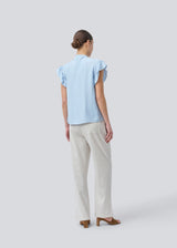 HolidayMD top in light blue is designed with a standing collar and button closure in front. The top has a frilly detail along the placket and at the armholes. The model is 175 cm and wears a size S/36.