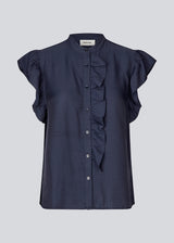 HolidayMD top in navy blue is designed with a standing collar and button closure in front. The top has a frilly detail along the placket and at the armholes. 