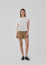 Top in white in broderie anglaise cotton with cutline below the chest with extra volume. HollynMD top has a round neck, short sleeves, and a small opening at the neck with button closure. The model is 175 cm and wears a size S/36.