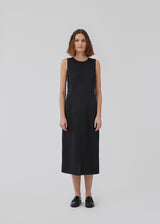 Dress in black with a slim silhouette, round neck, and without sleeves. HomerMD dress has an elegant look with a cutline mid front and back, and a high slit in front. Hidden zipper in the back. The model is 175 cm and wears a size S/36.
