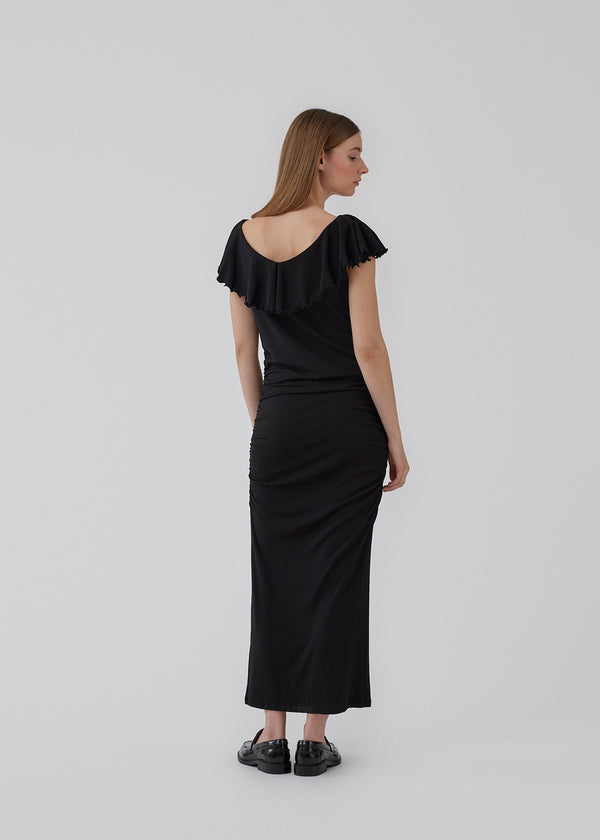 Close fitting dress cutting at a midi length. HugoMD dress has a wide and deep neckline in front and back with a tall frilly detail, and elasticated ruching at the sides. The model is 175 cm and wears a size S/36.