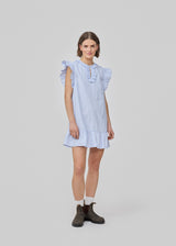 Short, sleeveless dress with ruffle details. The InaraMD dress has an opening in the front with a and button closure and decorative ruffles. The model is 177 cm and wears a size S/36