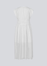 Sleeveless white maxi dress with a loose fit. IndiaMD dress has a deep v-neckline and a tie band at the waist and under the chest. The model is 177 cm and wears a size S/36.