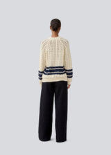 Loose knitted cardigan in beige with navy blue stripes in the button in cable knit. MetteMD cardigan is slightly see-through and has loose sleeves and a button closure. The models are 177 cm and wear a size S/36. 