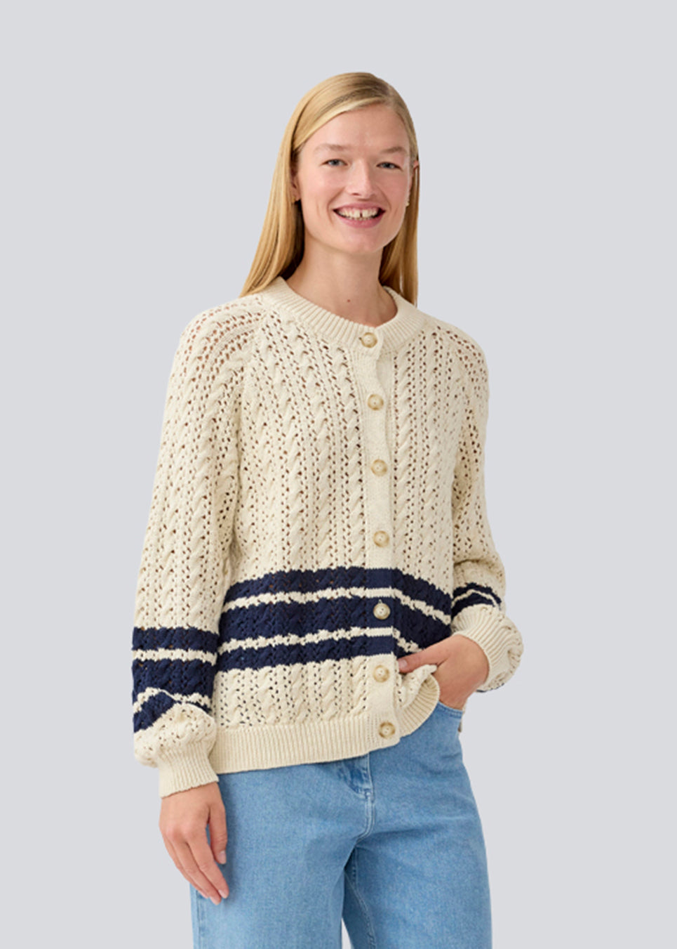 Loose knitted cardigan in beige with navy blue stripes in the button in cable knit. MetteMD cardigan is slightly see-through and has loose sleeves and a button closure. The models are 177 cm and wear a size S/36. 