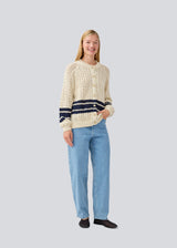 Loose knitted cardigan in beige with navy blue stripes in the button in cable knit. MetteMD cardigan is slightly see-through and has loose sleeves and a button closure. The models are 177 cm and wear a size S/36. 