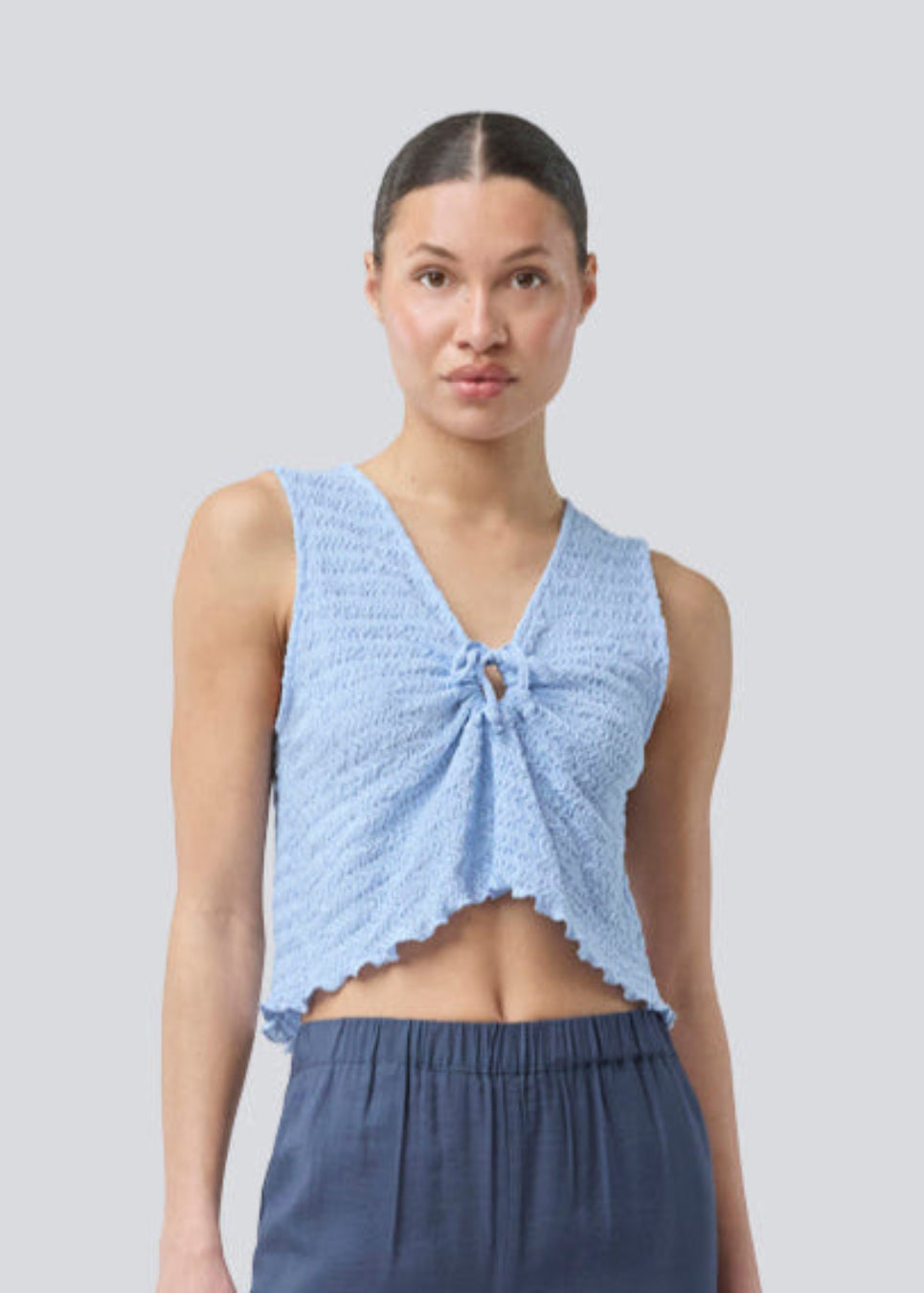 Sleeveless blue top with an opening with a tiedetail in front. NolineMD top is slightly cropped and has a loose fit and v-neck.