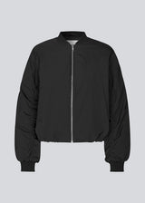 Padded black bomber jacket with gatherings at the sleeves. Obimd jacket is slightly cropped and has a zipper closure and two front pockets. 