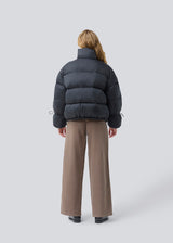 Black puffer jacket with a high neck in 100% recycled polyester. Odinmd jacket has a zipper closure and an adjustable strap at the sleeve. The model is 175 cm and wears a size s/36.