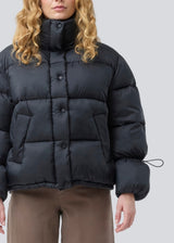 Black puffer jacket with a high neck in 100% recycled polyester. Odinmd jacket has a zipper closure and an adjustable strap at the sleeve. The model is 175 cm and wears a size s/36.