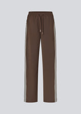 Loose brown trousers with wide legs and a relaxed fit. Featuring an elastic waistband with drawstring for a comfortable, adjustable waist. White side stripes add a sporty and modern touch to the otherwise classic design. Perfect for casual everyday wear or more elevated styling – easy to pair with everything from t-shirts to dressy tops.