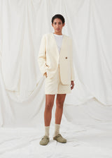 DimeMD blazer is designed in a textured cotton blend with lining. The blazer is collarless but has an asymmetrical wrap detail with a single visible button. The model is 177 cm and wears a size S/36. Style the blazer with matching shorts: DimeMD shorts.