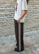 Loose brown trousers with wide legs and a relaxed fit. Featuring an elastic waistband with drawstring for a comfortable, adjustable waist. White side stripes add a sporty and modern touch to the otherwise classic design. Perfect for casual everyday wear or more elevated styling – easy to pair with everything from t-shirts to dressy tops.