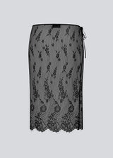 A square, sheer lace scarf worn as a wrap skirt. The Taffymd waist scarf ties at the side and is styled over trousers as part of the layered look trend.