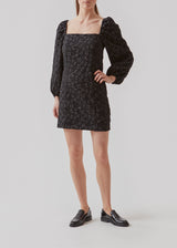 Short dress in black with all-over floral structure. AtiraMD dress has long balloon sleeves and a more fitted body. The neckline is square in front and back.