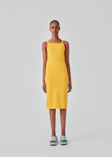 Tight fitted basic yellow dress in organic cotton jersey. DaeMD dress is sleeveless with a high and straight neckline. The dress cuts below the knees. The model is 177 cm and wears a size S/36.