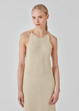 Open knit dress in beige in organic cotton. DariaMD dress has a slim fit with a long skirt, and straps that ties over the shoulder. The model is 177 cm and wears a size S/36.