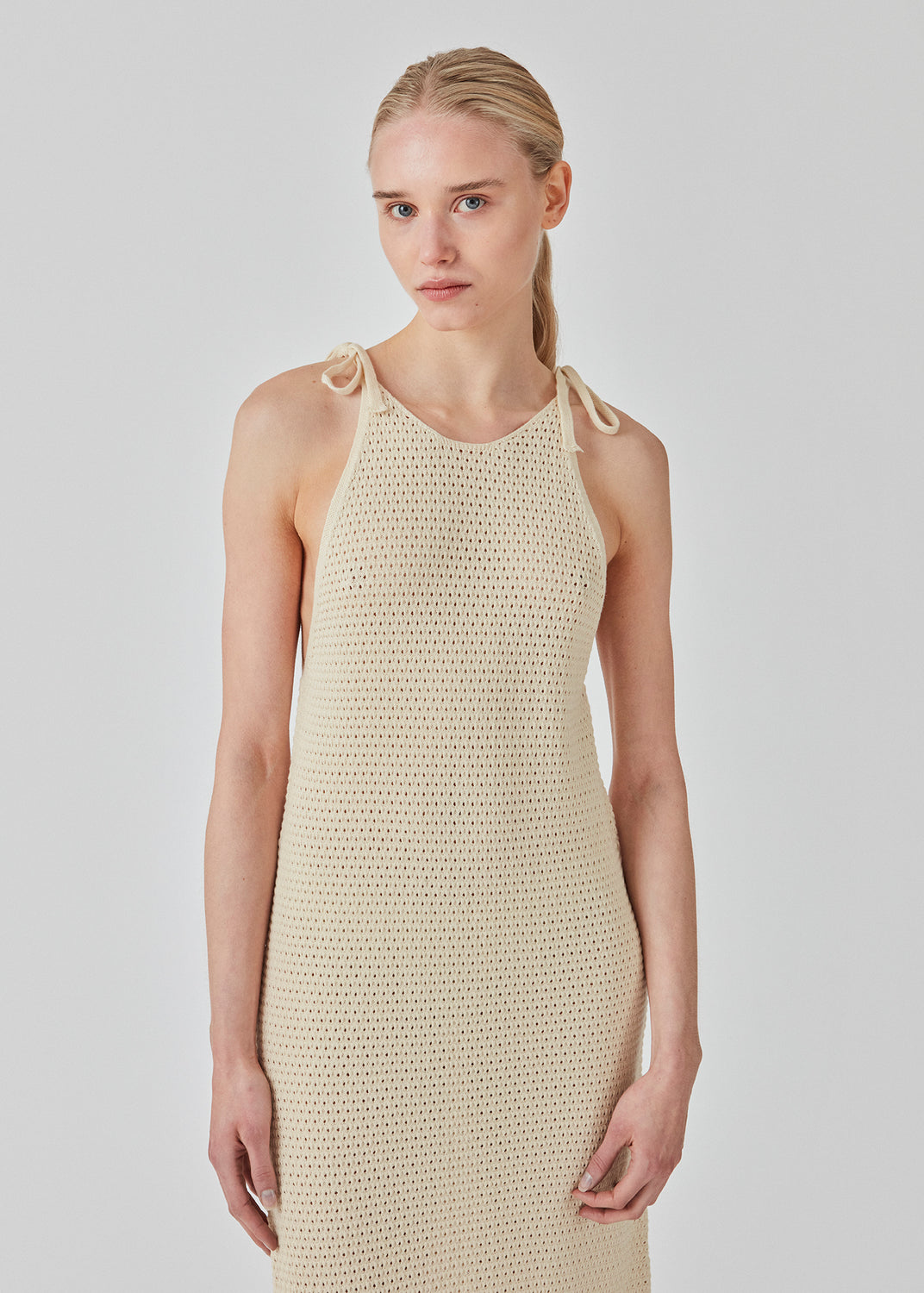 Open knit dress in beige in organic cotton. DariaMD dress has a slim fit with a long skirt, and straps that ties over the shoulder. The model is 177 cm and wears a size S/36.