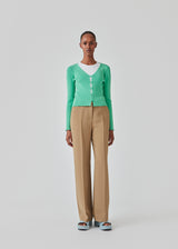 Slim fitted, slightly cropped cardigan in green with buttons at the front. DorisMD cardigan has a deep and round neckline, long sleeves, and lettuce hems. The model is 177 cm and wears a size S/36.