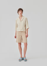 GaleMD shorts in beige have a classic design. The shorts cuts at knee-length, and have wide legs with creases for an elegant look. The model is 173 cm and wears a size S/36.  Buy Gale blazer in the same color that fits the shorts.