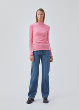 Tight fitted t-shirt in pink with a medium high neck. Issy t-neck has feminine lettuce hem on neck and sleeves. The quality is a soft jersey with a feminine pointelle pattern.