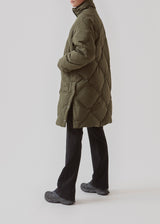Quilted jacket with down filling i green. ScarlettMD jacket is knee length with a high stand-up collar and a zipper with wind flap with press-studs. The jacket has two patch pockets with press studs in front and an elasticated cuff. The model is 177 cm and wears a size S/36.