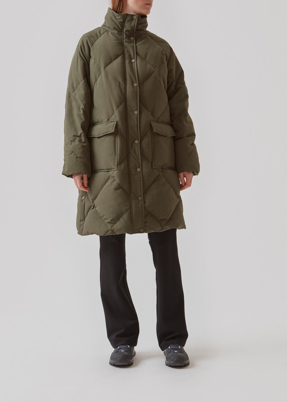 Quilted jacket with down filling i green. ScarlettMD jacket is knee length with a high stand-up collar and a zipper with wind flap with press-studs. The jacket has two patch pockets with press studs in front and an elasticated cuff. The model is 177 cm and wears a size S/36.