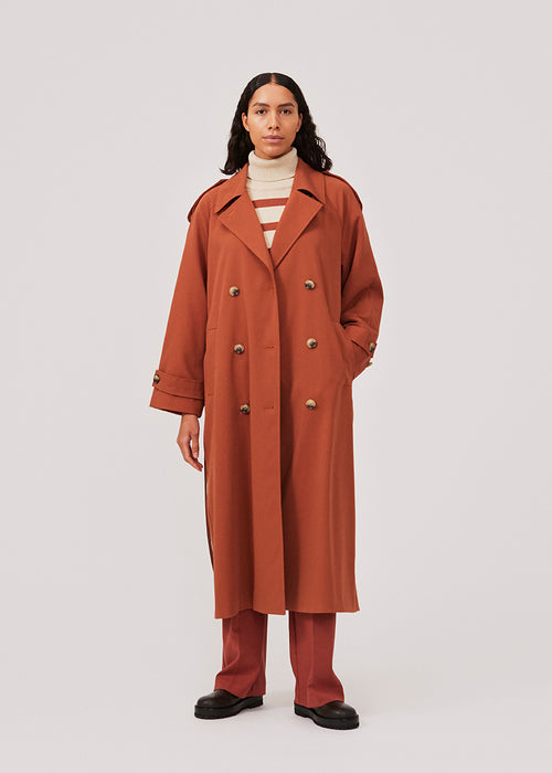 Oversized double-breasted trench coat in the color Maple with tie belt at the waist. EvieMD jacket has dropped shoulders and long, wide sleeves. Lined. The model is 175 cm and wears a size S/36.