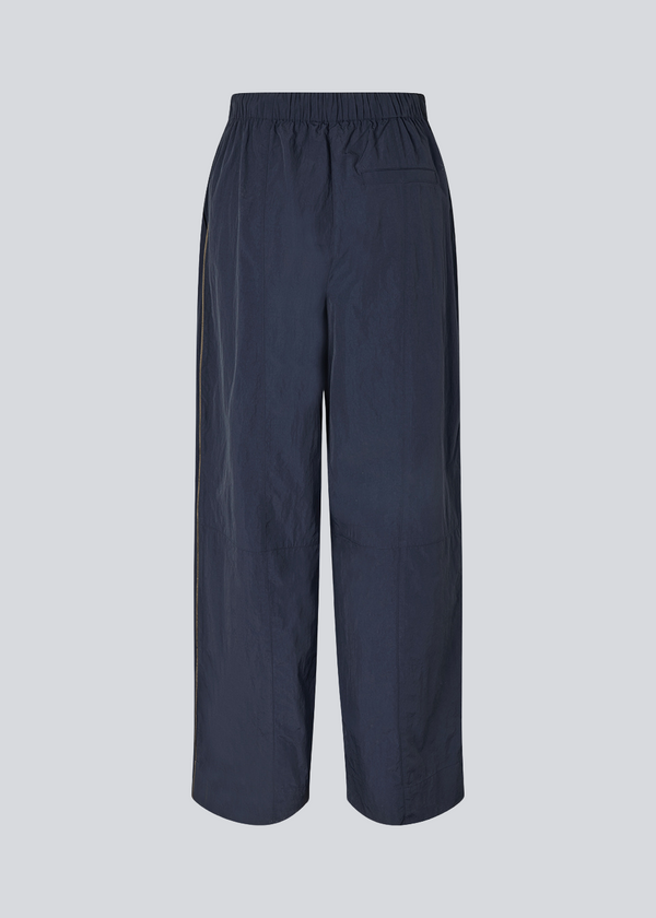 Dark blue tracksuitpants in 100% recycled nylon. Volmermd pants has piping along the sideseam and cutline details for a sporty look.