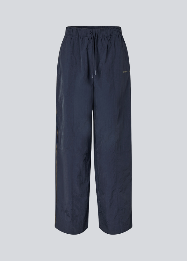 Dark blue tracksuitpants in 100% recycled nylon. Volmermd pants has piping along the sideseam and cutline details for a sporty look.