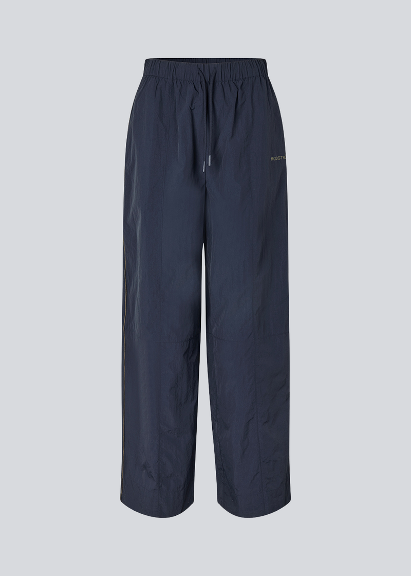 Dark blue tracksuitpants in 100% recycled nylon. Volmermd pants has piping along the sideseam and cutline details for a sporty look.