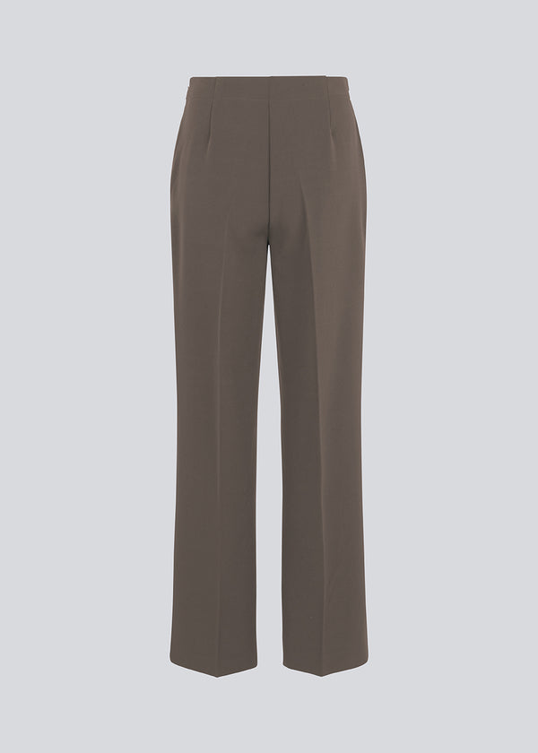 Classic pants in brown with pressfolds and straight legs. Nelli pants are closed by an hidden zipper at the side with an elastic waistband for a more comfortable fit.&nbsp;