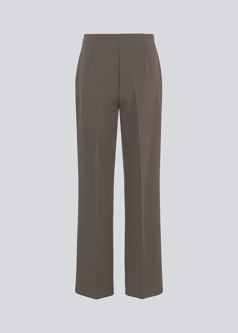 Classic pants in brown with pressfolds and straight legs. Nelli pants are closed by an hidden zipper at the side with an elastic waistband for a more comfortable fit.&nbsp;